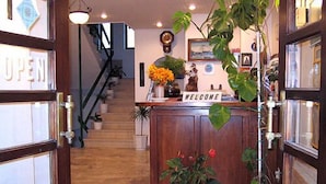 A reception area with a wooden desk, a 'WELCOME' sign, potted plants, and a staircase in the background. - Hotel Doxa (Agios Nikolaos)