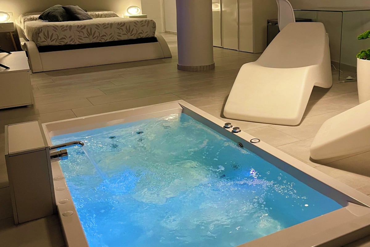 Een moderne spa ruimte met een jacuzzi, een massagestoel en een bed met nachtkastje.