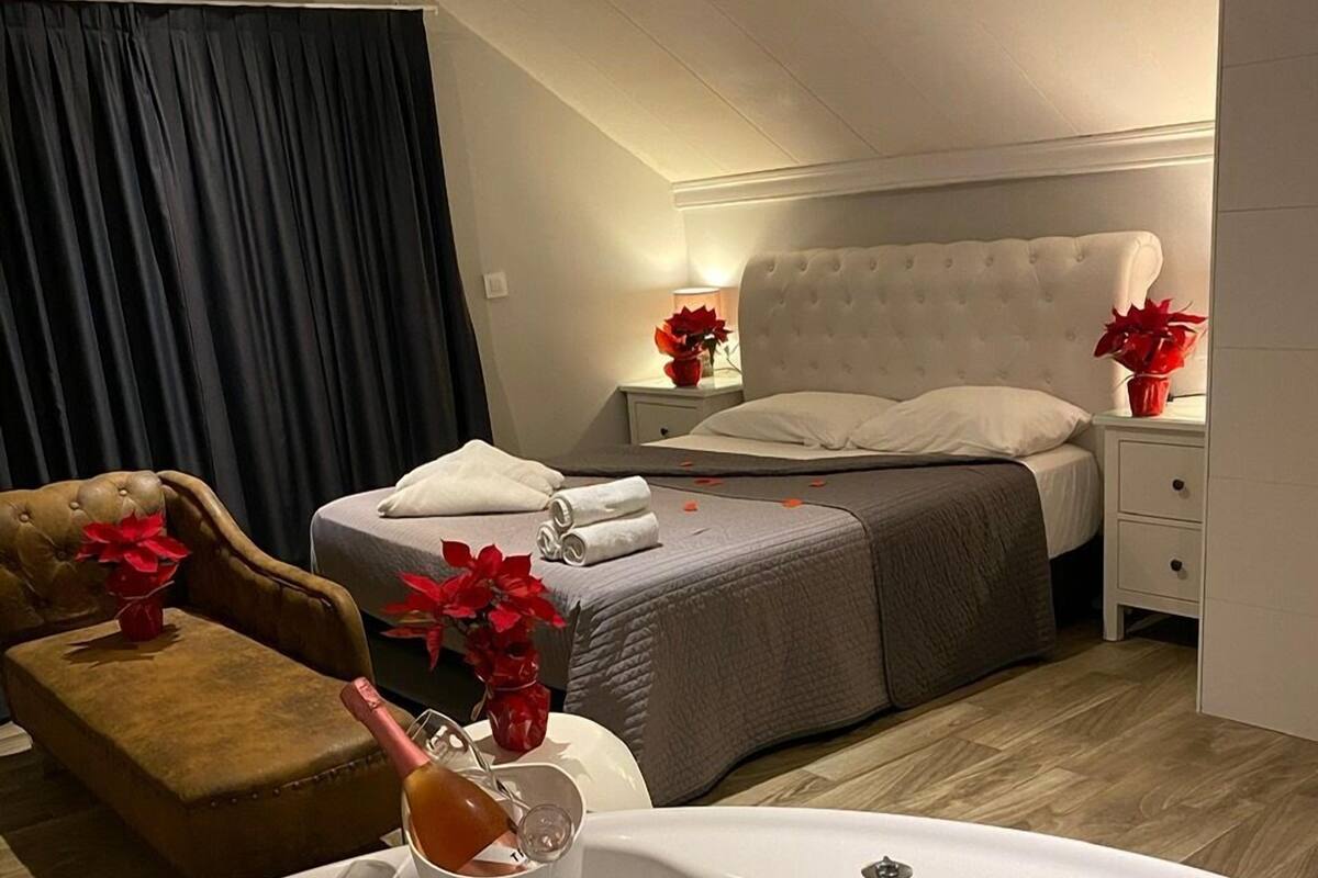 Hotelkamer met een groot bed, een zithoek met een bruine fauteuil, een wit bad met rozenblaadjes en een minibar.