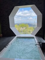 Uma banheira de hidromassagem com vista para uma paisagem montanhosa através de uma janela geométrica.