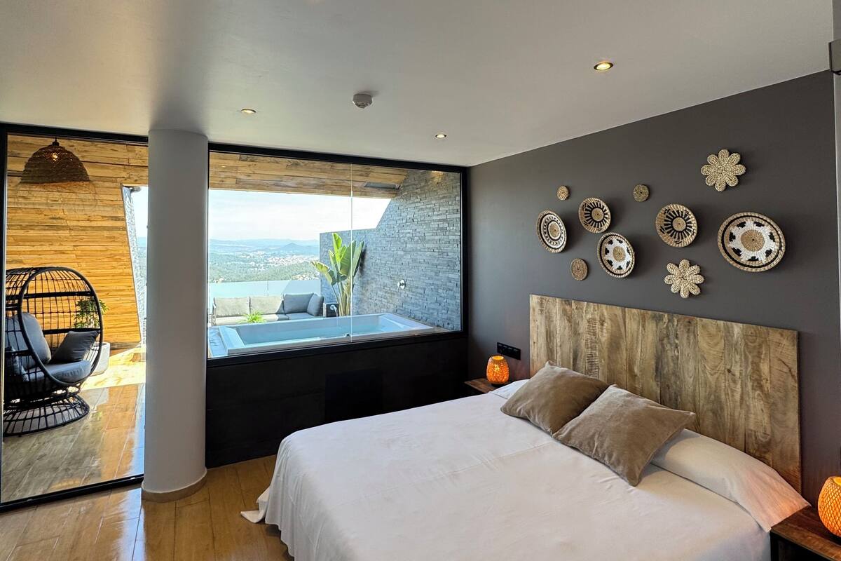 Een moderne slaapkamer met een groot bed, uitzicht op de omgeving en decoratieve muurkunst.