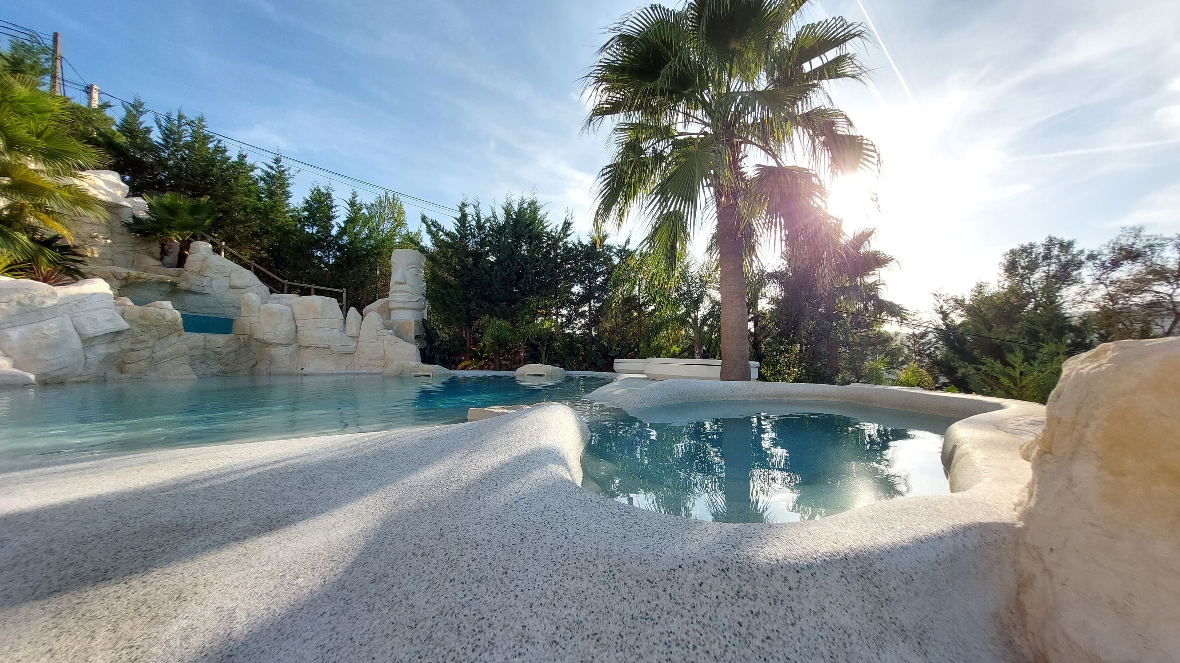 A pool area with clear water, surrounded by rock formations and palm trees.