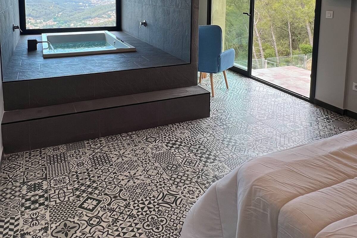 Een moderne badkamer met een groot bad, uitzicht op het landschap en een vloer met een patroon.