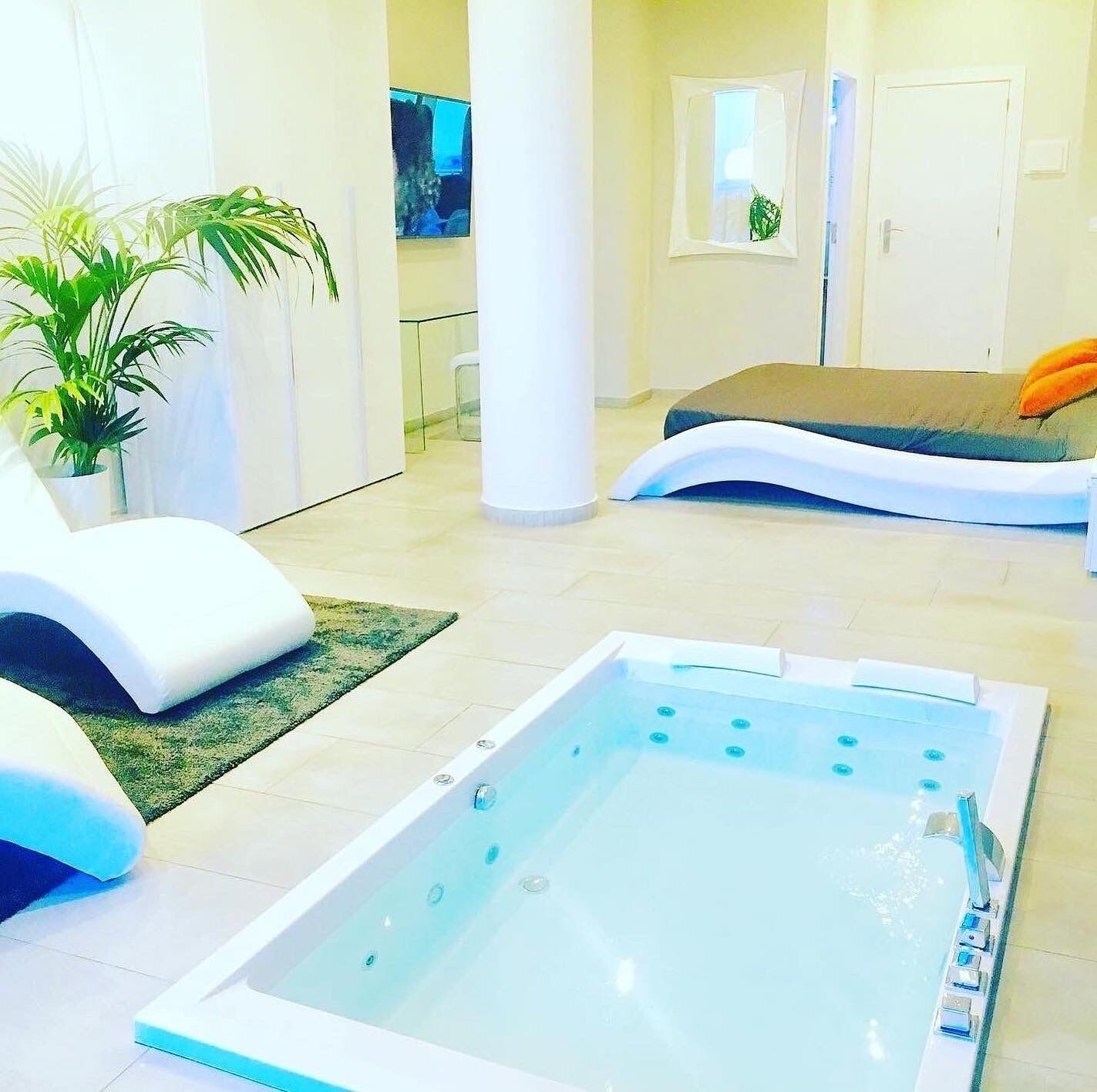 Un área de piscina interior moderna con un jacuzzi, sillones de descanso y una planta grande en maceta.