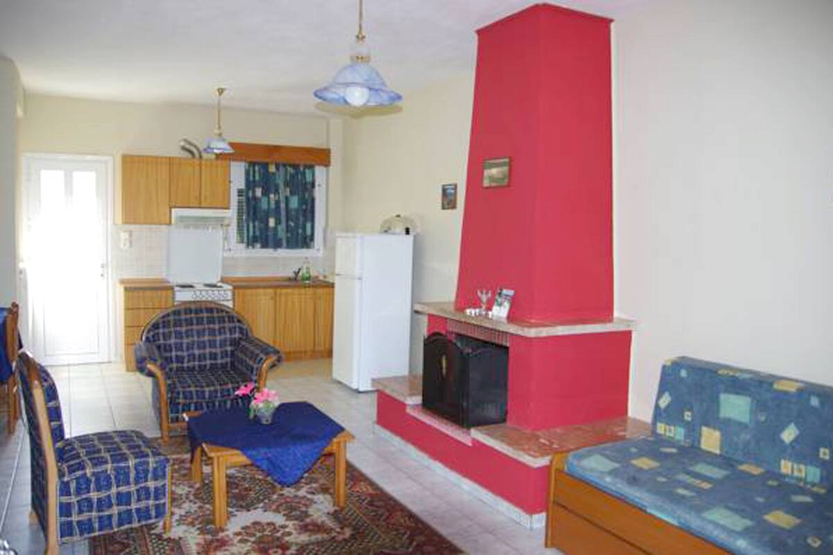A living room with a red fireplace, a dining area with wooden furniture, and a kitchen with wooden cabinets and a window.