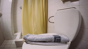 Un baño con inodoro blanco, cortina de ducha amarilla y piso de baldosas.