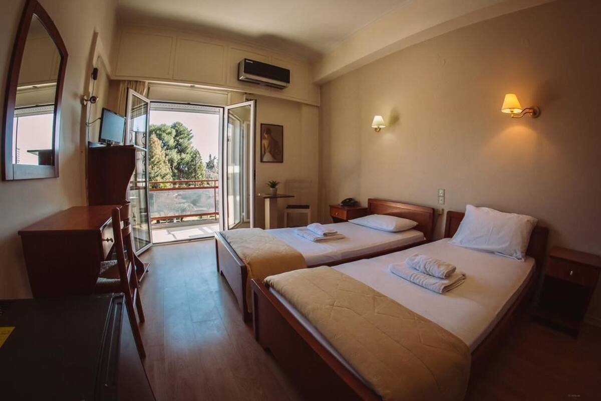 Ein Hotelzimmer mit zwei Betten, einem Schreibtisch, einem Sessel, einem Fernseher und einem Balkon mit Blick.