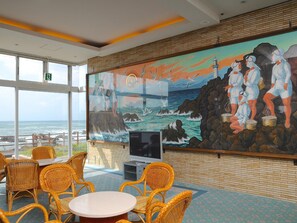 A room with wicker furniture, a large mural of seascapes, and a television.