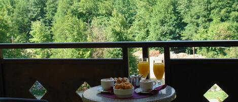 A balcony with a table set for breakfast, overlooking a forested valley.