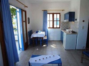 A compact kitchen with a dining area, a small table with a white tablecloth, and a window with curtains. - Hotel Agnanti (Milos)