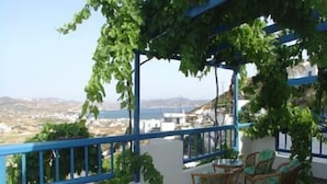 A terrace with a pergola covered in green vines, a table with chairs, and a view of the sea and distant landscape. - Hotel Agnanti (Milos)