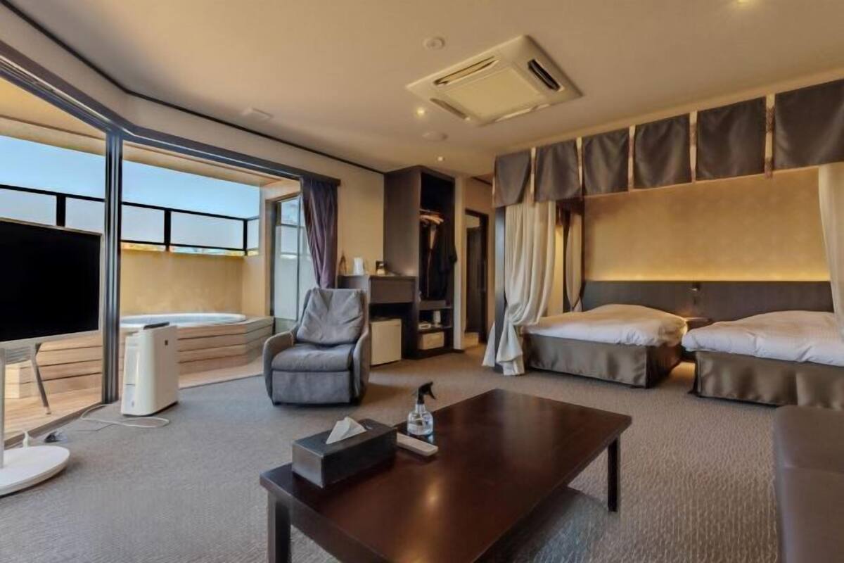 Ein modernes Hotelzimmer mit großem Fenster, Flachbildfernseher, Sofa, Bett und Couchtisch.