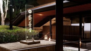 A modern building with a wooden exterior, a glass entrance, and a stone pathway leading to a wooden door. - Saiou No Miya (Ise)