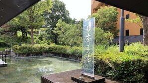 A courtyard with a water feature, a stone pedestal with a sign, and surrounding greenery. - Saiou No Miya (Ise)