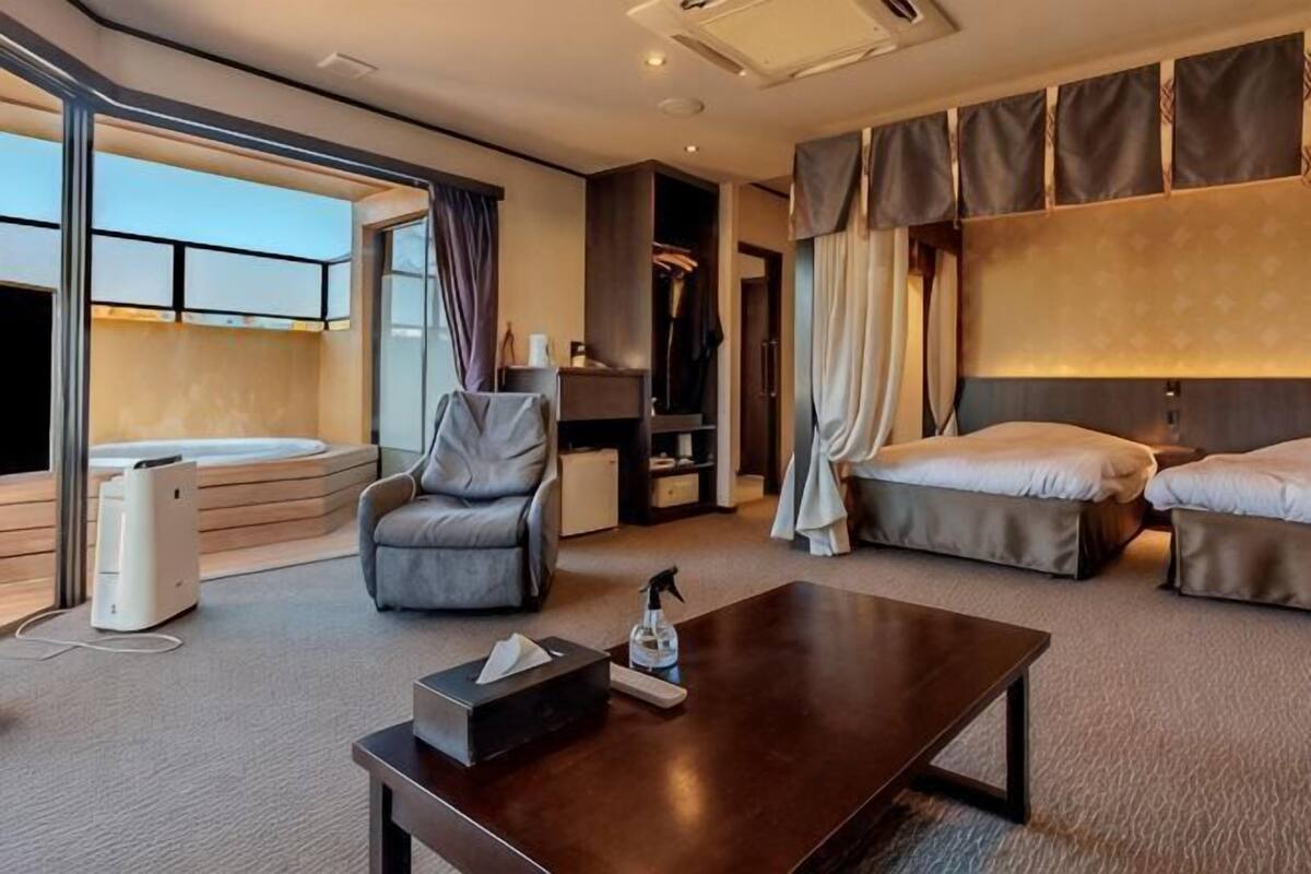 Ein Hotelzimmer mit einer Couch, einem Couchtisch, einem Fernseher, einem Bett und einem Balkon.