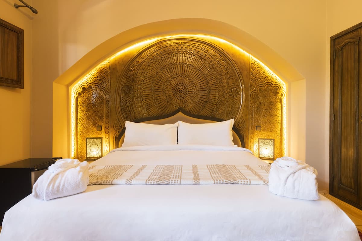 A hotel room with a large bed, ornate headboard, and two bedside lamps.