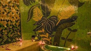 Une salle de bain avec un mur décoré de mosaïques, une baignoire et des pétales de rose éparpillés sur le sol.