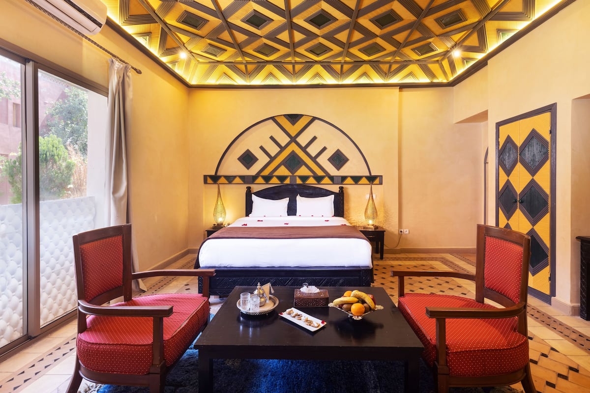 A hotel room with a bed, two armchairs, a coffee table with breakfast items, and a decorative ceiling.