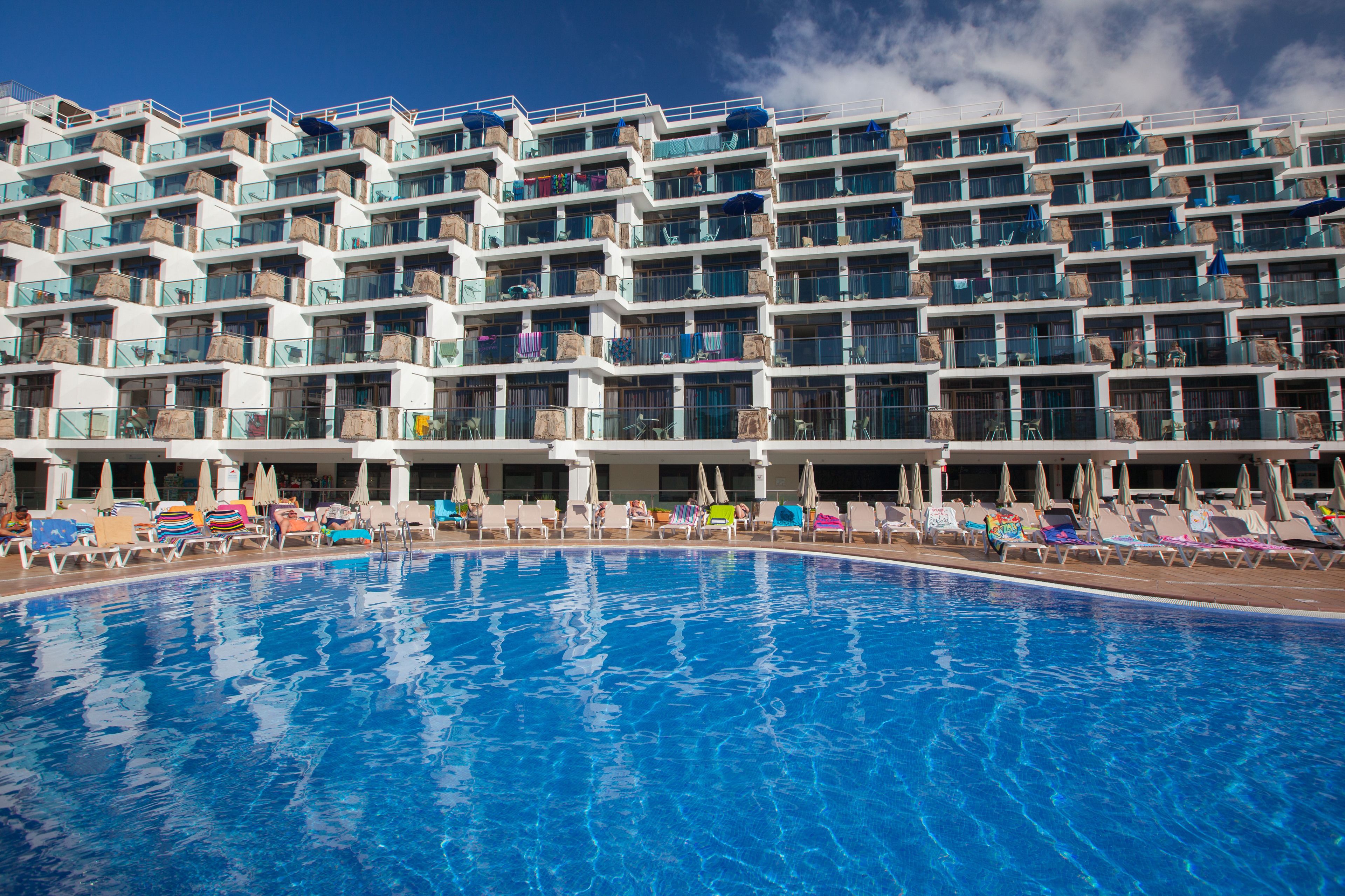 A hotel with a large swimming pool, multiple balconies, and sun loungers.