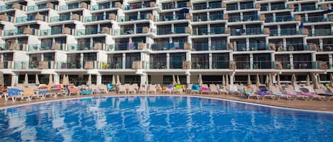 A hotel with a large swimming pool, multiple balconies, and sun loungers.
