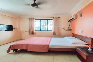 Quarto com cama, televisão, janela com cortinas, ar-condicionado e ventilador de teto.