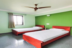 A room with two single beds, a ceiling fan, a window with curtains, and a green wall. - Siesta de Goa (Varca)