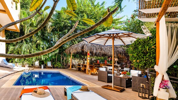 Un área junto a la piscina con sillas de descanso, una sombrilla de paja y mobiliario exterior.