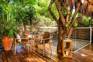 Una terraza de madera con una mesa y sillas, rodeada de abundante vegetación y un árbol con frutos verdes.