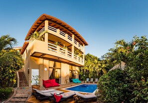 Una casa de dos pisos con piscina, mobiliario exterior y una escalera que lleva al nivel superior.