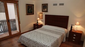 A bedroom with a large bed, two bedside tables, a wooden headboard, and a balcony with a glass door.