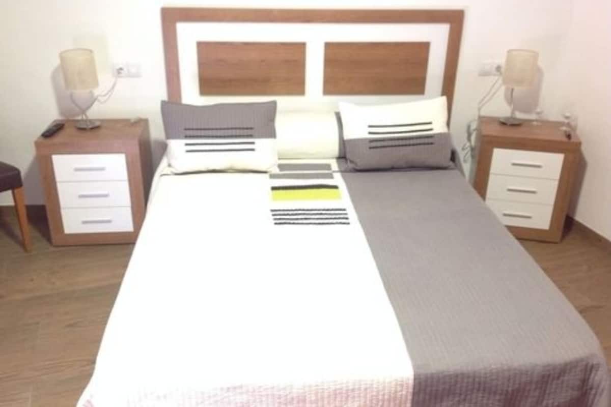 A neatly made bed with a wooden headboard, two bedside tables with lamps, and a bedside drawer.