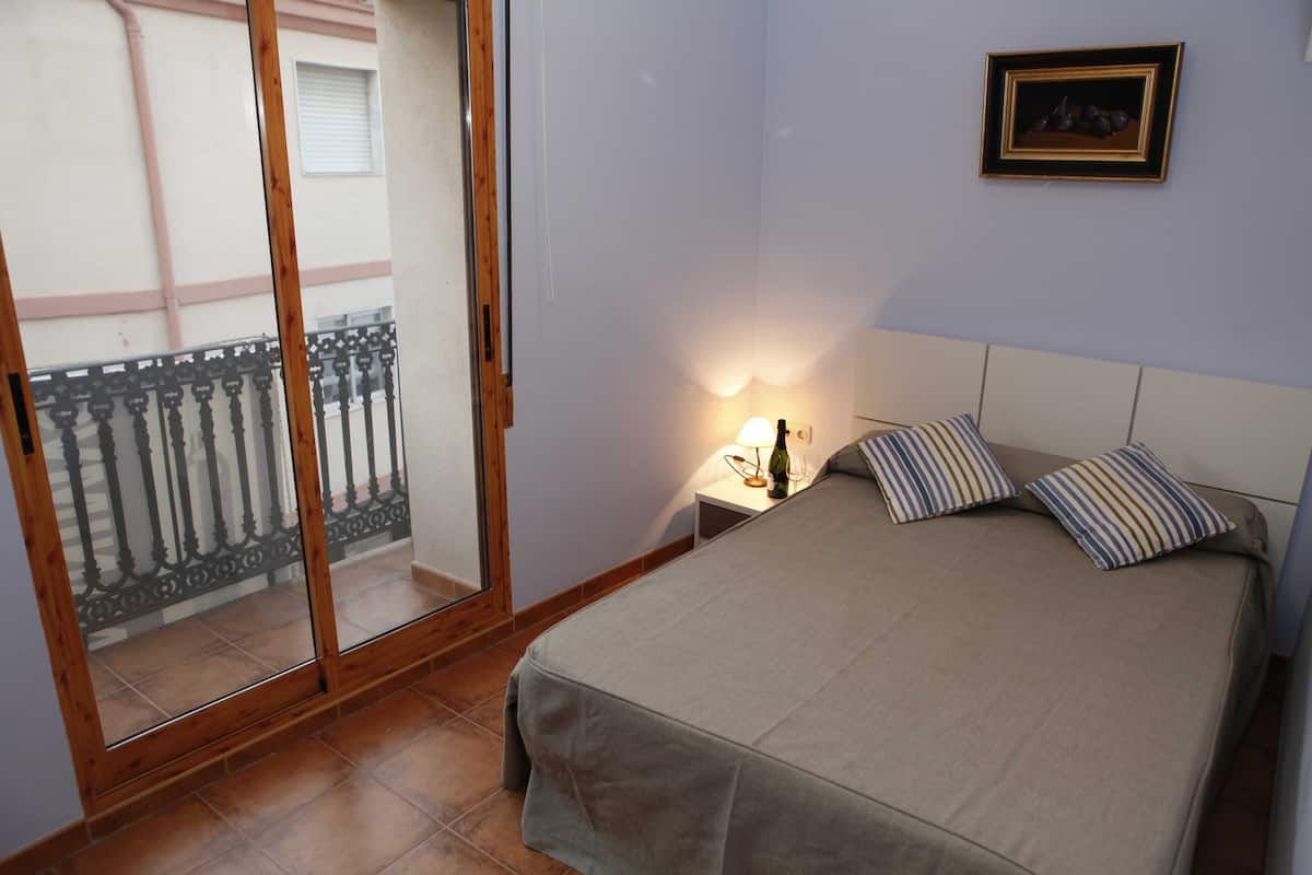 A bedroom with a bed, a nightstand, a lamp, a framed picture, and a sliding glass door leading to a balcony.