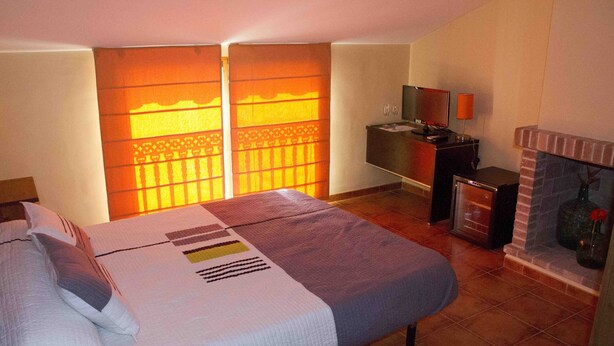A hotel room with a bed, a small desk, a television, and a fireplace.