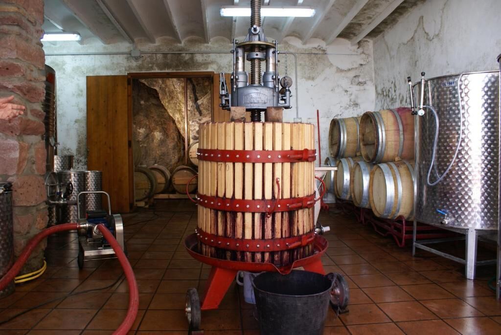 A barrel aging facility with wooden barrels, stainless steel tanks, and a mechanical press.