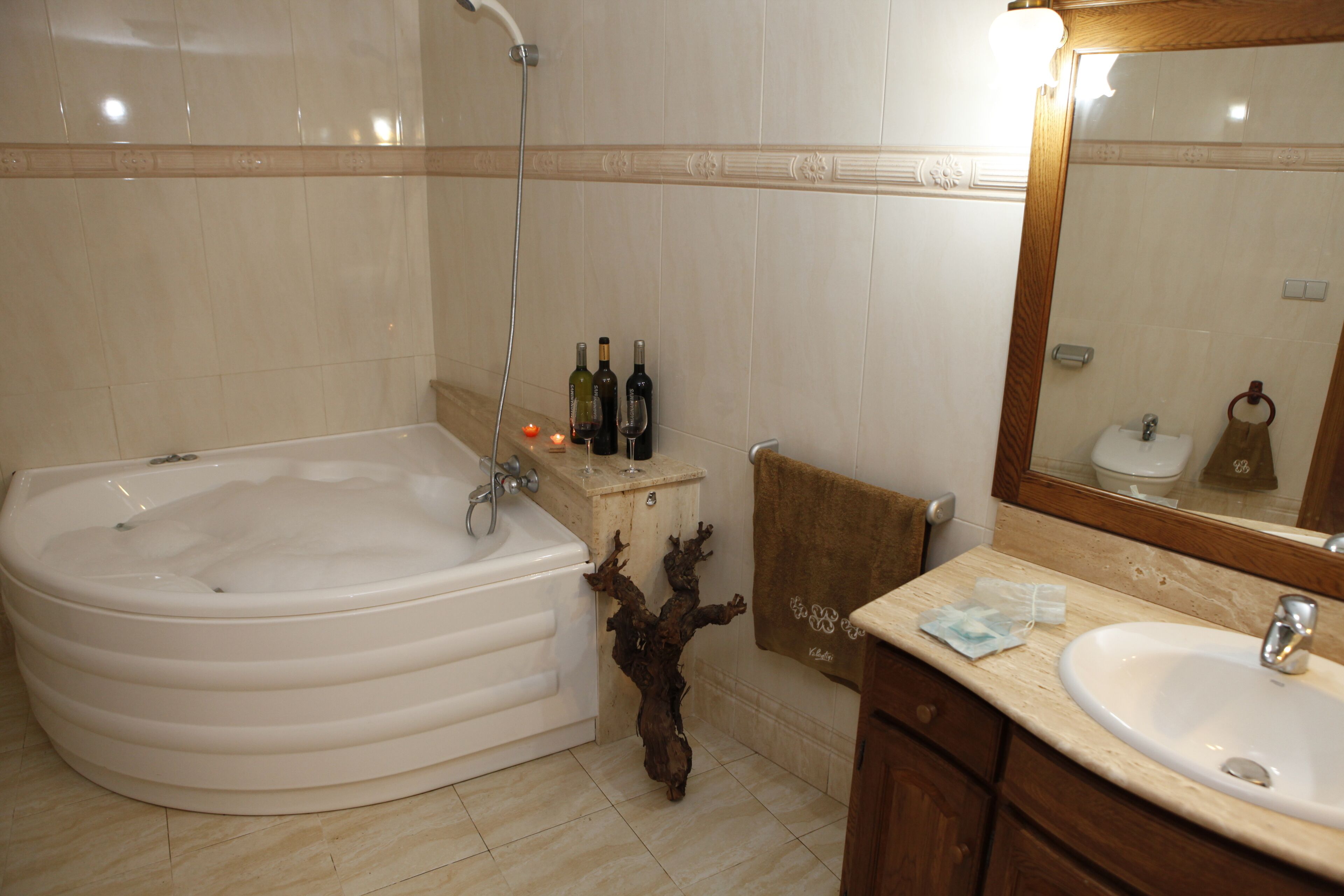 A bathroom with a large bathtub, a sink, and a mirror. There are bottles on the counter and a towel hanging on the wall.
