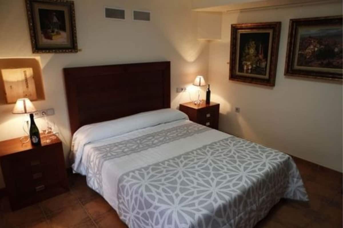 A bedroom with a large bed, a wooden headboard, two bedside tables with lamps, and framed pictures on the walls.