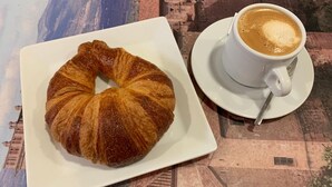 A croissant and a cup of coffee on a table with a cityscape backdrop.