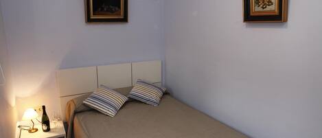 Un dormitorio con una cama, una mesita de noche, una lámpara, una botella y dos cuadros en la pared.