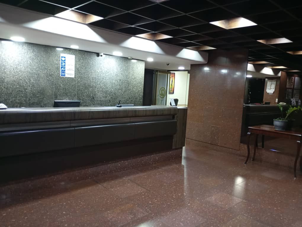 Un área de recepción con mostrador de mármol, un cubo de basura y una planta en maceta.