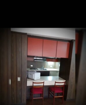 A compact kitchen with red cabinets, a white countertop, and two wooden chairs. - Cuarta Avenida Suites (Caracas)
