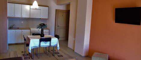 A compact living space with a dining area, kitchen, and a TV mounted on the wall.