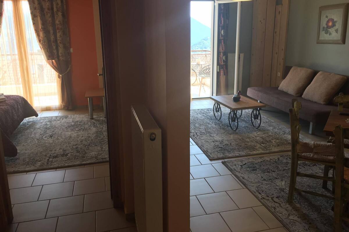 Ein Zimmer mit einem Bett, einem kleinen Tisch, einer Couch und einem Sessel. Eine Tür führt in einen weiteren Raum.