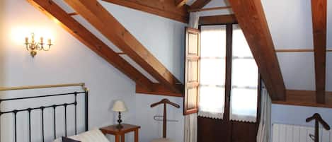 Un dormitorio con cama, mesita de noche, silla, techo de madera y ventana con cortinas.