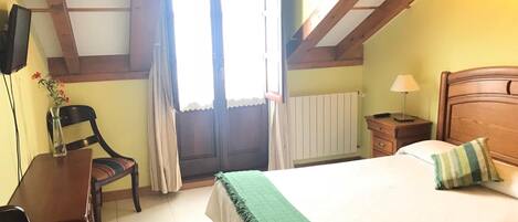 A bedroom with a bed, a desk, a chair, a nightstand, and a window with curtains.