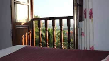 Una habitación con cama, ventana y vistas a palmeras y edificios.