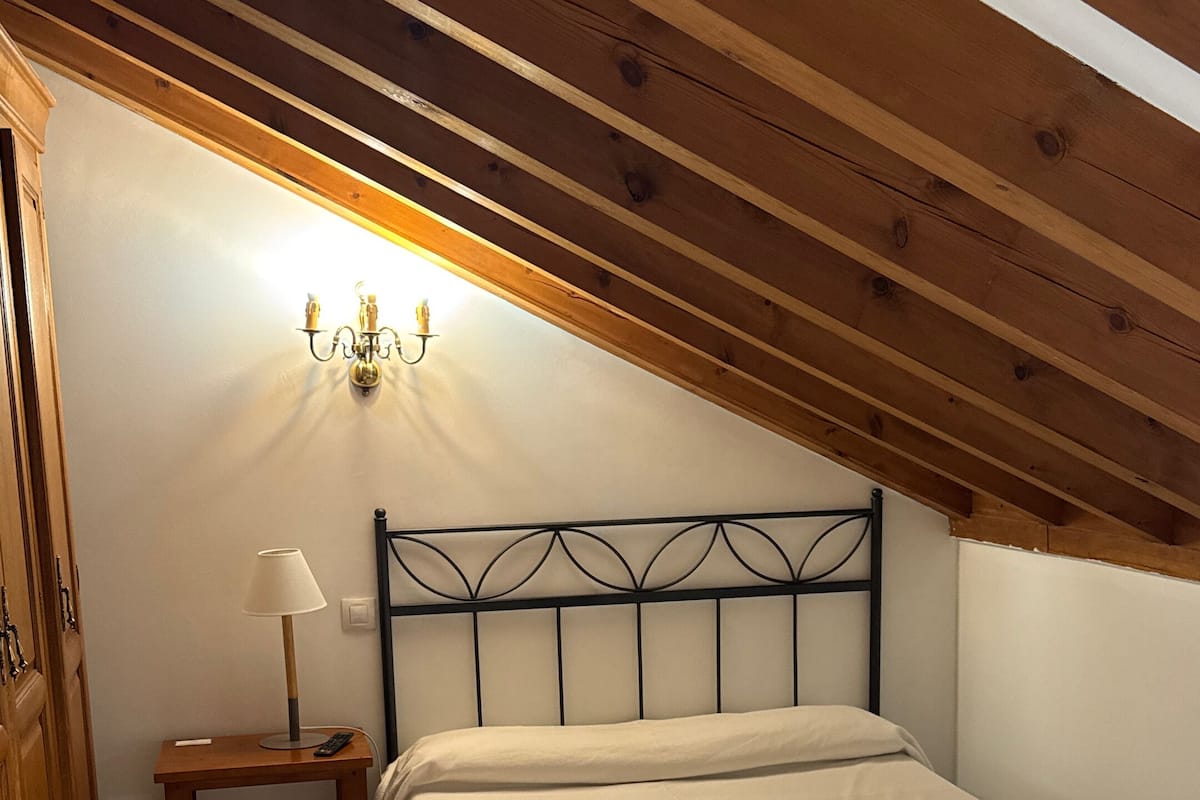 A bedroom with a bed, a nightstand, a lamp, and a wall-mounted light fixture.