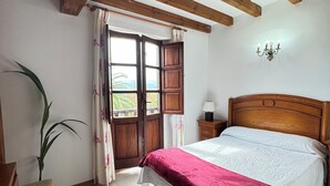 A bedroom with a wooden bed, a nightstand, a chair, a potted plant, and a window with curtains.