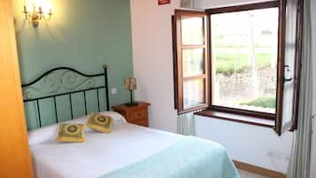 A bedroom with a bed, a nightstand, a wall-mounted lamp, and a window with curtains.
