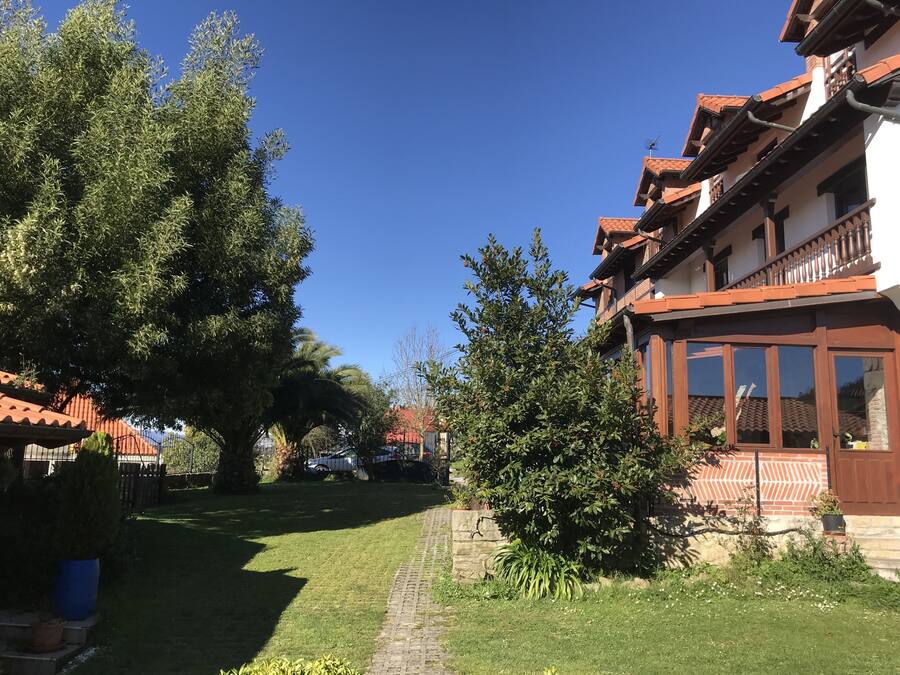 A courtyard with a paved path, surrounded by trees and a building with a red-tiled roof and wooden balconies.