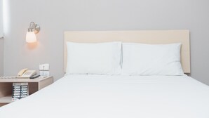 Ett hotellrum med en säng, ett nattduksbord med en telefon och en lampa samt en väggmonterad lampa.